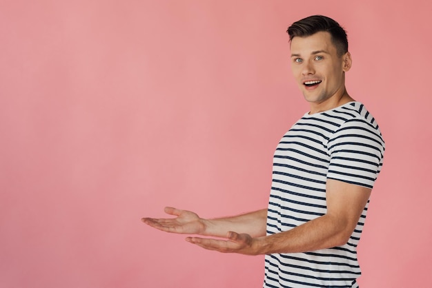 Photo smiling man in striped tshirt pointing with hands isolated on pink