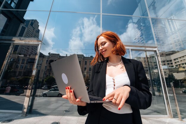 Фото Улыбающаяся женщина смотрит на свой ноутбук на открытом воздухе, современный образ жизни