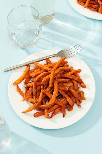 Sweet potato fries and glass on blue background with long shadows in minimal style