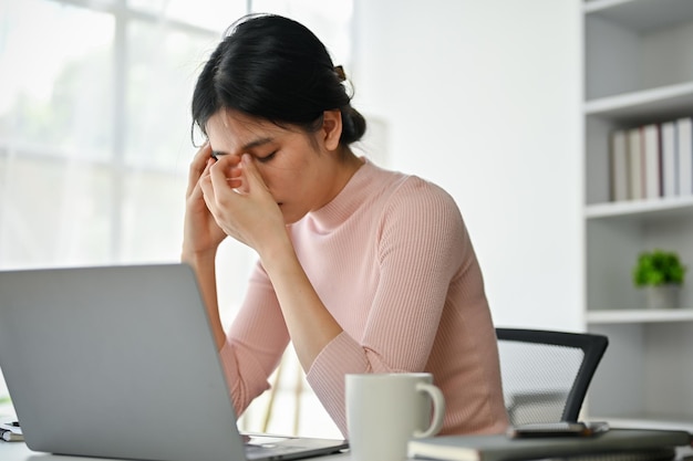 Стрессовая азиатская деловая женщина страдает от головных болей, беспокоясь о своей работе