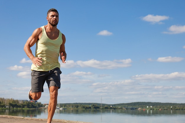 Foto forte uomo sportivo che fa jogging mentre si allena vicino al lungofiume della città.