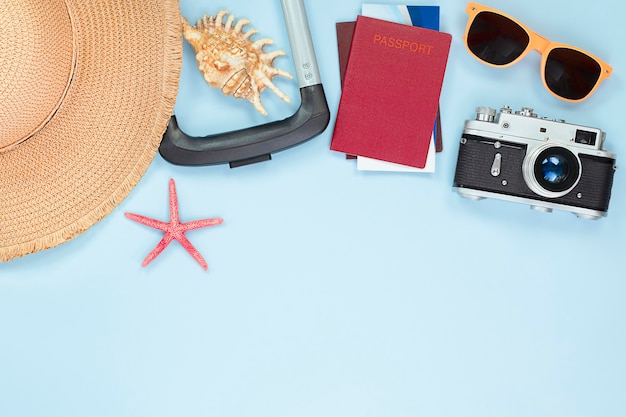 사진 밝은 파란색 배경에 태양 모자, 여행 가방, 조개, 불가사리, 티켓, 여권, 안경 및 카메라. 여행 컨셉