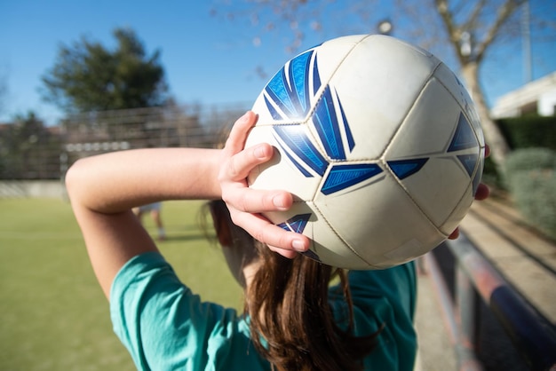 Close-up van tienermeisjes handen met bal. Achteraanzicht van jong meisje met witte en blauwe bal boven haar hoofd op schoolstadion, klaar om het naar haar vriend te gooien. Damesvoetbal, concept voor een gezonde levensstijl