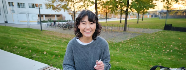 Gratis foto jonge koreaanse kunstenaar of kunststudent zit in het park met digitale tablet en tekent met grafische pen