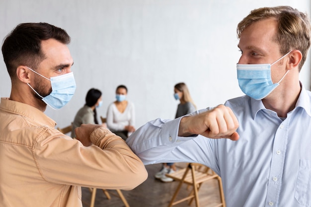 Mannen met medische maskers tijdens een groepstherapiesessie die de ellebooggroet doen