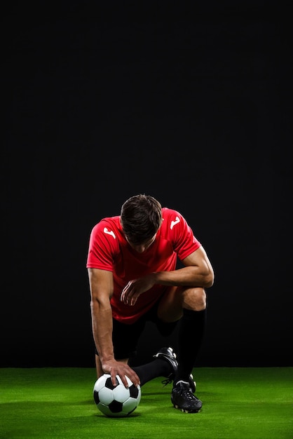 Gratis foto voetballer met bal die zich op één knie over zwarte backgrou bevindt