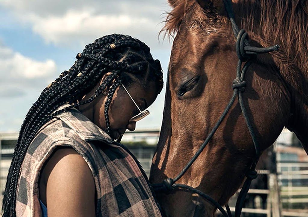 A Black woman standing face-to-face in front of her horse in a peaceful moment.