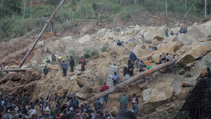 Dozens of people clamber of large boulders and soil searching for people trapped under rubble