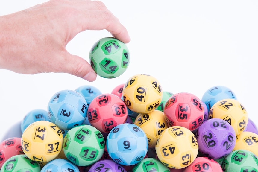 A photo of colourful lottery balls stacked on top one another with a hand grabbing the top green ball