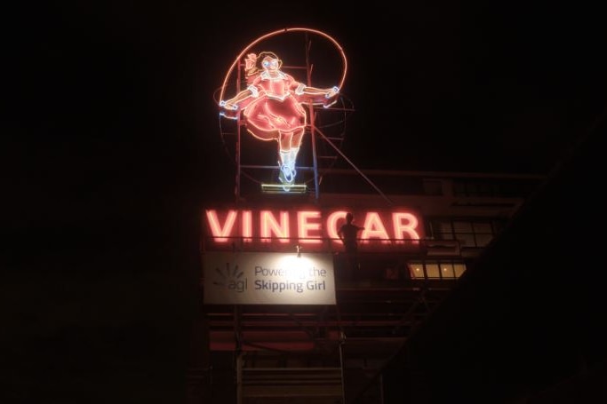 A neon sign in red and white featuring a girl skipping.
