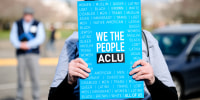 A person holds a blue sign that reads "We The People ACLU"