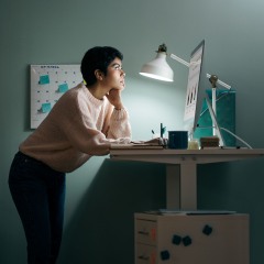 Young woman standing on desk using computer and working after hours at home office.