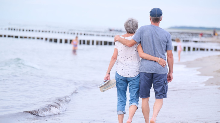 Zeit für die schönen Dinge des Lebens: Ein Rentnerehepaar geht am Strand Arm in Arm spazieren.