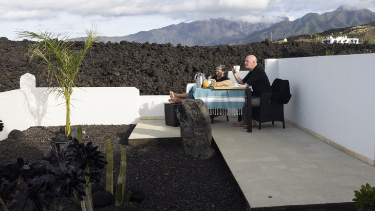 Deutsche Touristen frühstücken auf der Terrasse ihres Gästehauses vor einem Lavafeld.