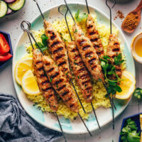 Chicken kofta kebabs on a plate over lemon rice with other items around it for serving