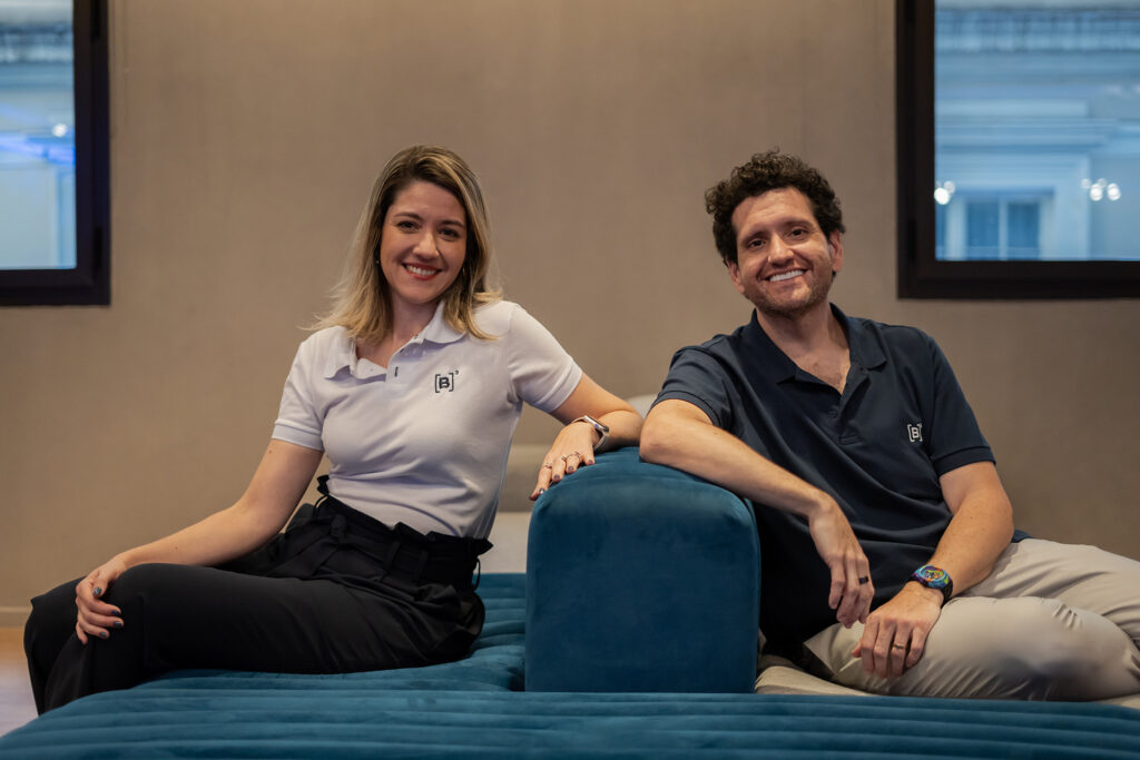 Christianne Bariquelli y Marcos Albino Rodrigues sentados en un sofá, frente a la cámara. Ambos sonríen y visten polos con el logo B3.