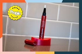 The Colgate Optic White Overnight Teeth Whitening Pen in a holder on a bathroom counter with a colorful border