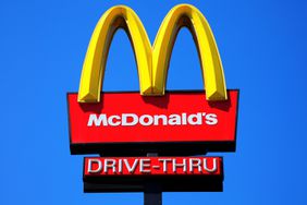 McDonald's yellow and red drive-thru logo advertising sign placed on a pole with a clear blue sky