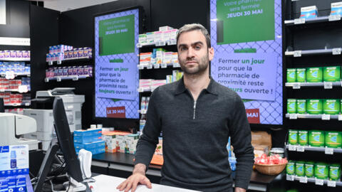 French musician, singer and pharmacist Julien Sfeir poses for a picture in front of screens announcing a pharmacists' strike in a pharmacy at Angers railway station, western France, on May 28, 2024.