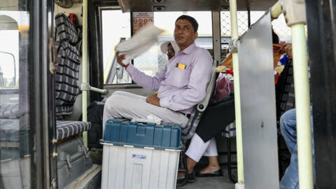 A polling official uses a cloth as a fan to cool off as he waits inside a bus with a Voter Verified Paper Audit Trail (VVPAT) machine outside a distribution center in Varanasi on May 31, 2024, on the 