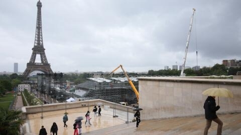 Pedestrians holding umbrellas walk past the temporary venue under construction for the upcoming Paris 2024 Olympic Games close to the Eiffel Tower on May 31, 2024.