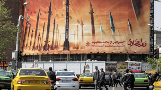 Motorists drive their vehicles past a billboard depicting named Iranian ballistic missiles in service, with text in Arabic reading "the honest [person's] promise" and in Persian "Israel is weaker than