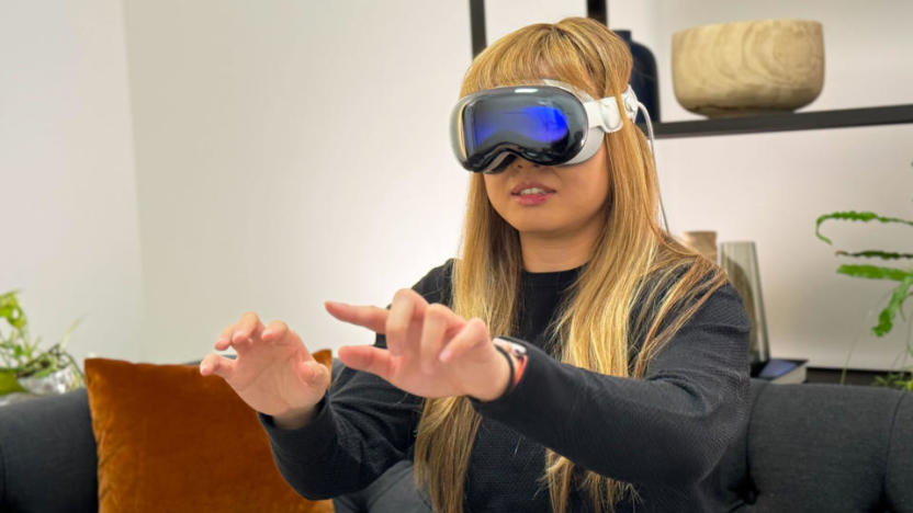 Photo of Engadget’s Cherlynn Low wearing the Apple Vision Pro headset. Her hands are outstretched in front of her as she sits on a modern office couch.
