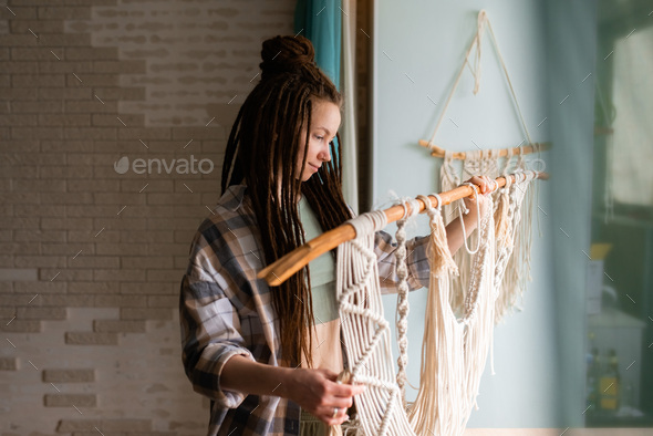 Young woman with dreadlocks weaves home decor from cotton thread macrame.  - Stock Photo - Images