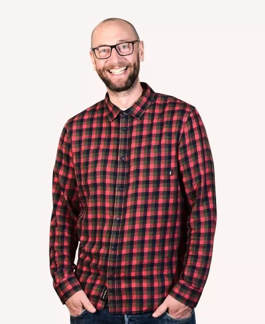 Andy smiles wearing a red checked shirt, he is very tall