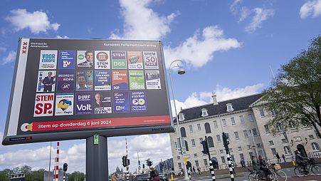 Ciclistas passam por um cartaz das eleições europeias em frente ao Museu Marítimo em Amesterdão, Países Baixos, quarta-feira, 5 de junho de 2024.