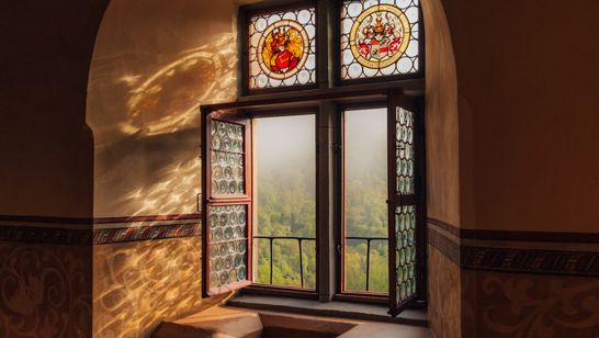 Licht scheint durch die geöffneten Fenster des Rittersaals mit Aussicht auf den Eifelwald