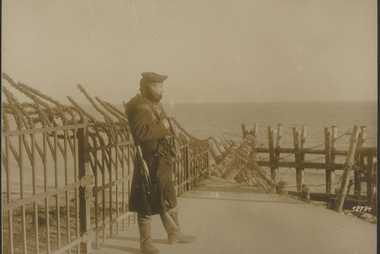 Bewaffneter Mann an einer Stützmauer am Meer.