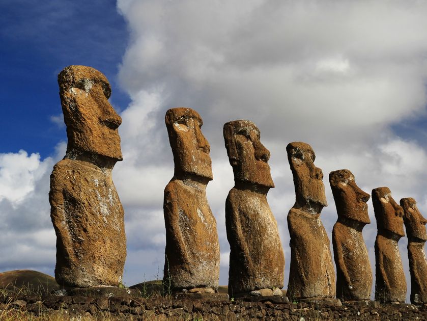 Sieben Moai Statuen stehen aufgereiht auf einer Steinplattform.